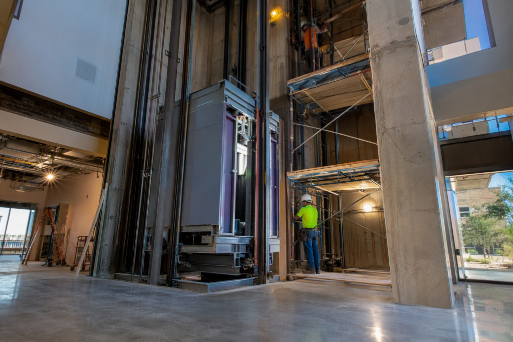 New commercial elevator installation in progress inside a Phoenix AZ mid-rise office building, showing hoistway, guide rails, and cab being set by technicians
