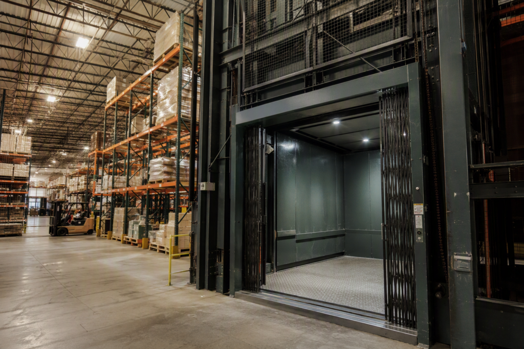 Heavy-duty freight elevator inside a multi-story Arizona warehouse facility showing industrial cab, steel mesh gate, and pallet racking — key equipment for warehouse vertical transport compliance.